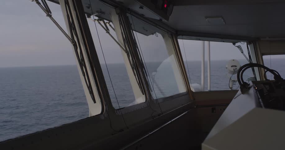 A static shot from the dark bridge of a ship as it sails across the calm ocean on an overcast day