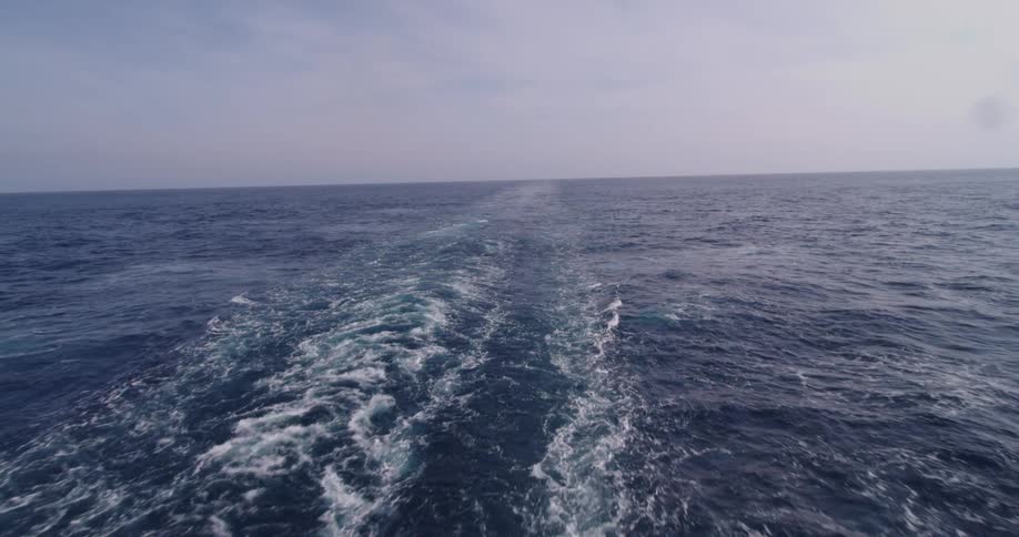 The wake of a ship trails behind as it sails across the vast open ocean under a hazy sky