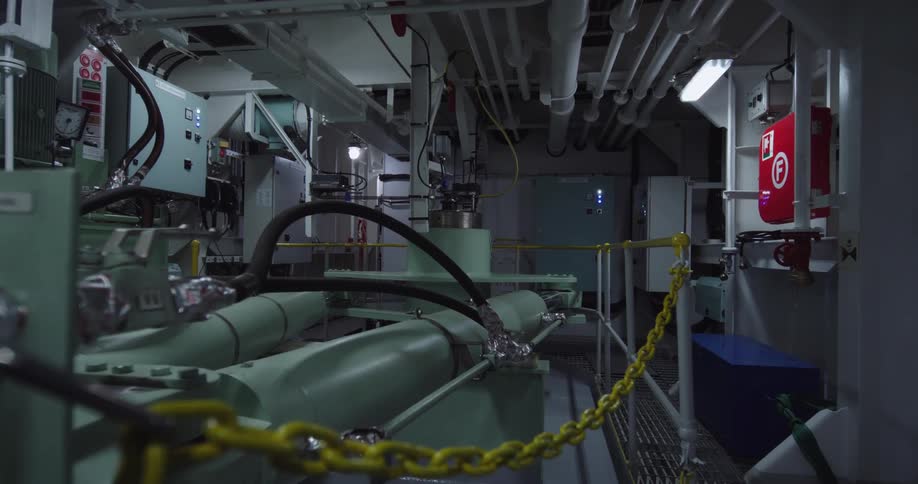Static view of an industrial ship's engine room with large machinery, pipes, and a yellow chain in the foreground