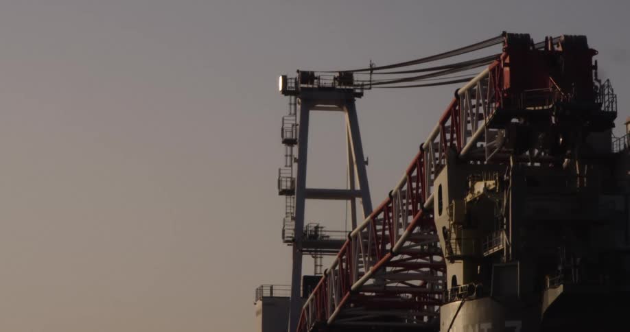 A close-up shot of a large industrial crane with a flashing beacon at dusk