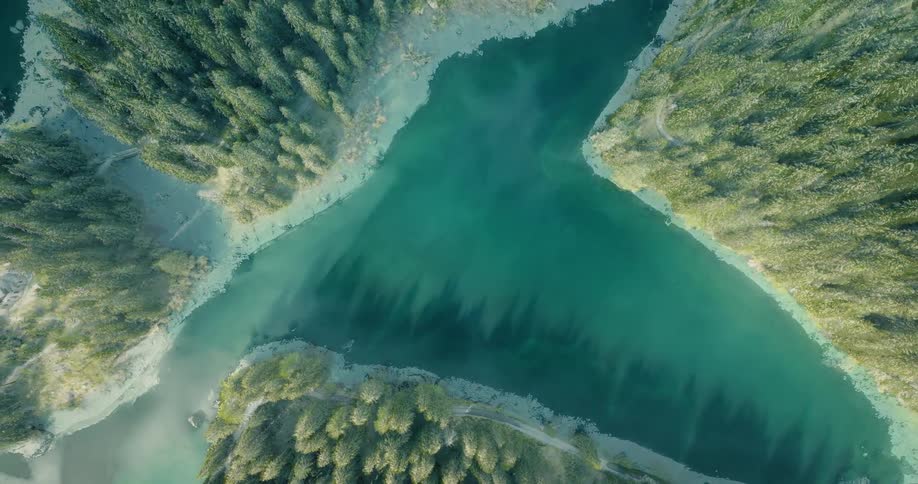 A stunning top-down aerial time-lapse captures the transition of a pristine mountain lake from a snow-covered winter landscape to a lush summer paradise