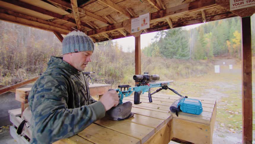 A man in camouflage prepares his modern, scoped rifle for target practice at an outdoor shooting range