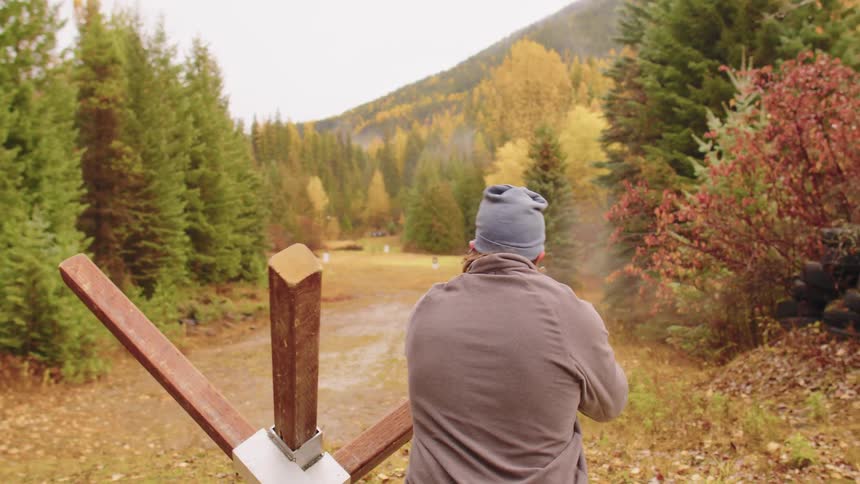 Slow motion shot of a man firing a scoped rifle from a barricade at an outdoor range in an autumn forest