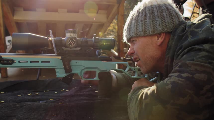 Close-up slow motion shot of a man in camouflage firing a precision rifle and adjusting the scope