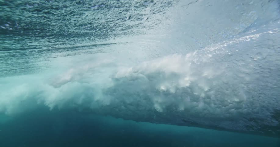 An immersive underwater slow-motion view captures the powerful energy of a breaking ocean wave from below