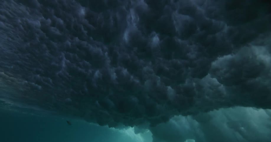 An underwater, slow-motion view of a powerful ocean wave as it rolls overhead, blocking out the sun and creating dark, turbulent textures