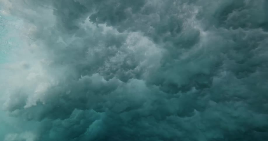 An immersive slow-motion underwater view looking up as a powerful ocean wave crashes and churns into turbulent white water