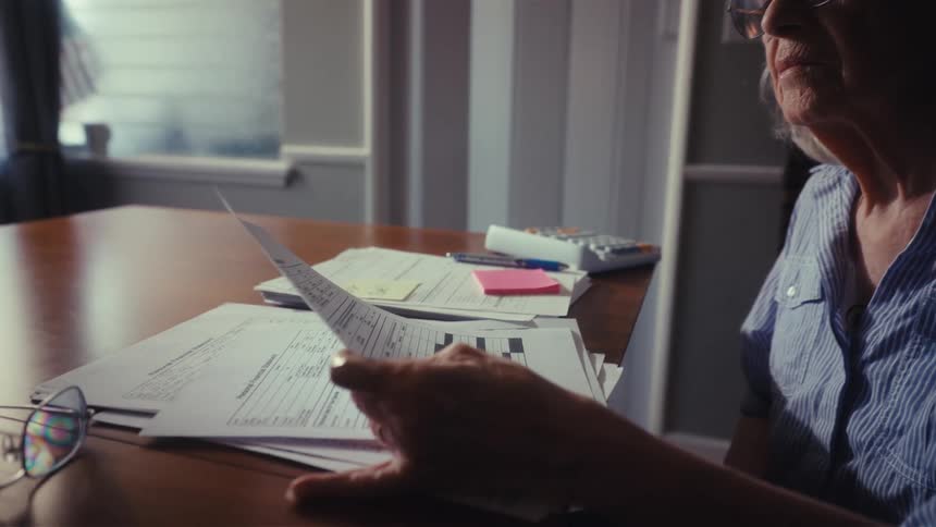 A concerned senior woman carefully examines her household bills and financial paperwork at home