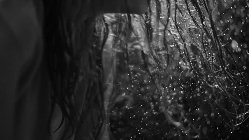 A dramatic black and white slow-motion close-up of water showering onto long, wet hair
