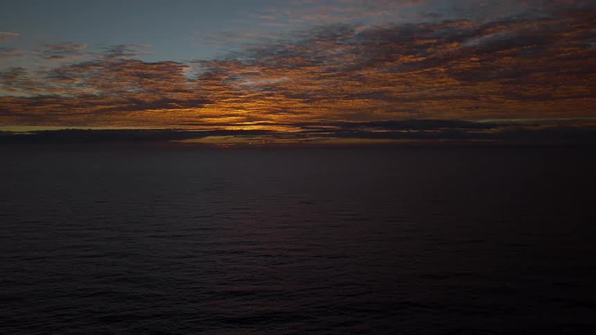 A serene view of the dark ocean under a magnificent sunset sky with golden clouds on the horizon