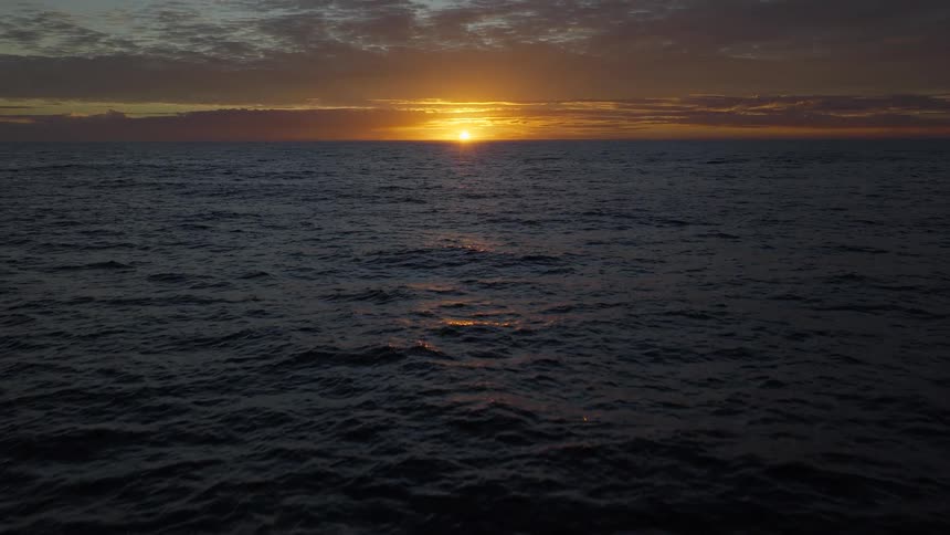 The golden sun dips below the horizon, casting a warm glow over the dark, endless ocean waves