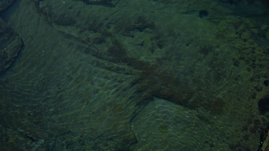Sunlight creates beautiful, abstract rippling patterns on the rocky floor of a tranquil, clear body of water