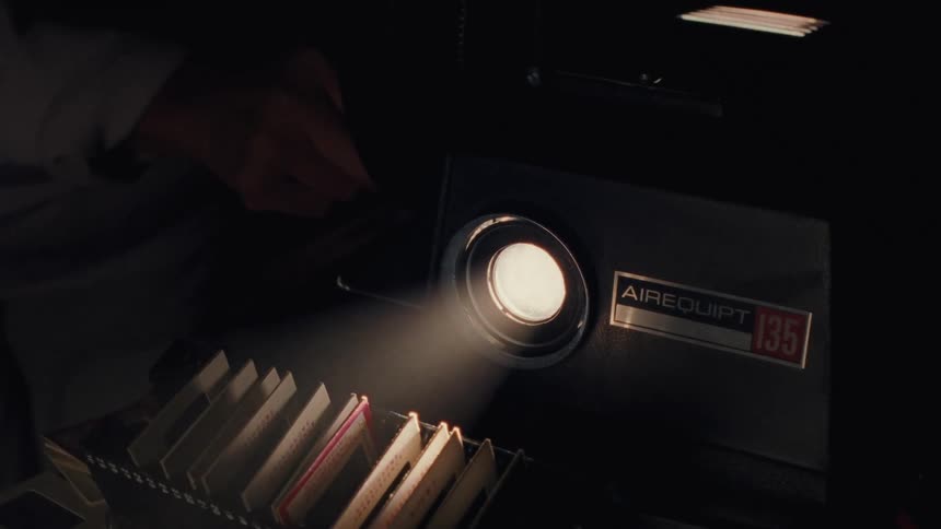 Close up of a vintage slide projector's light beam flickering as a person changes slides in a dark room