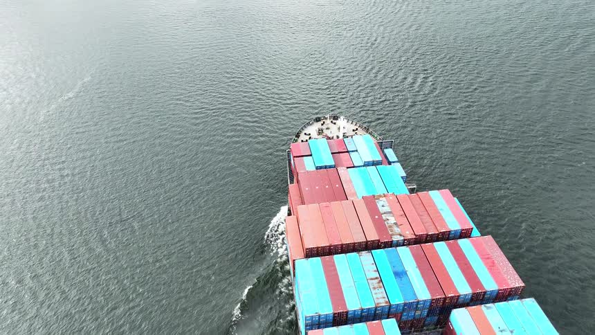 An aerial view from above shows a large container cargo ship sailing through the open water