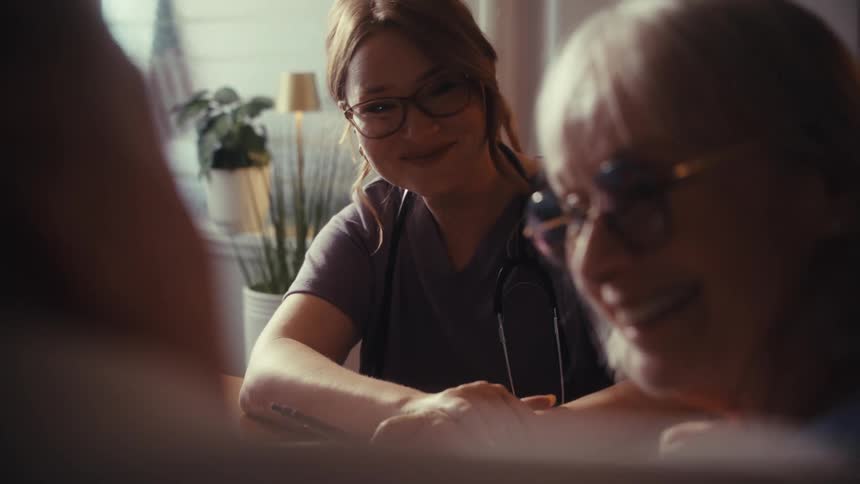 A compassionate nurse provides comfort and reassurance to a smiling elderly couple during a home visit