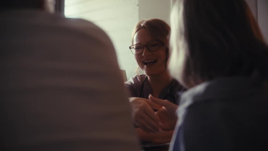 A compassionate female healthcare provider laughs and holds hands with a senior couple during a friendly in-home consultation