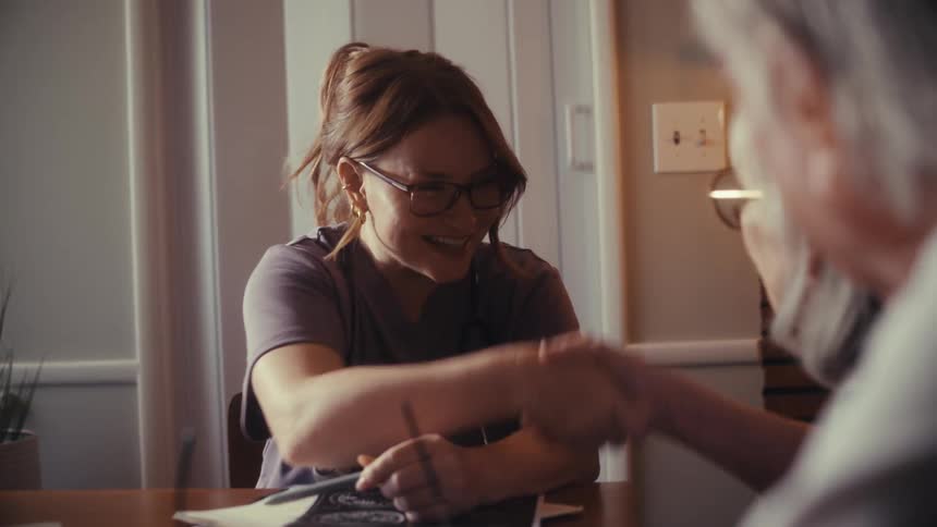 A smiling female nurse shakes hands with a senior couple during a friendly in-home healthcare consultation