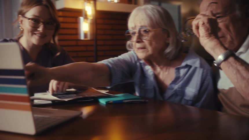 A caring female doctor consults with a concerned elderly couple in their home, explaining medical test results shown on a laptop