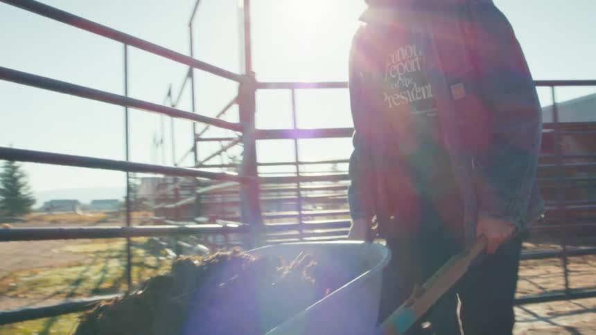 Slow motion shot of a rancher moving a wheelbarrow full of steaming manure on a sunny day
