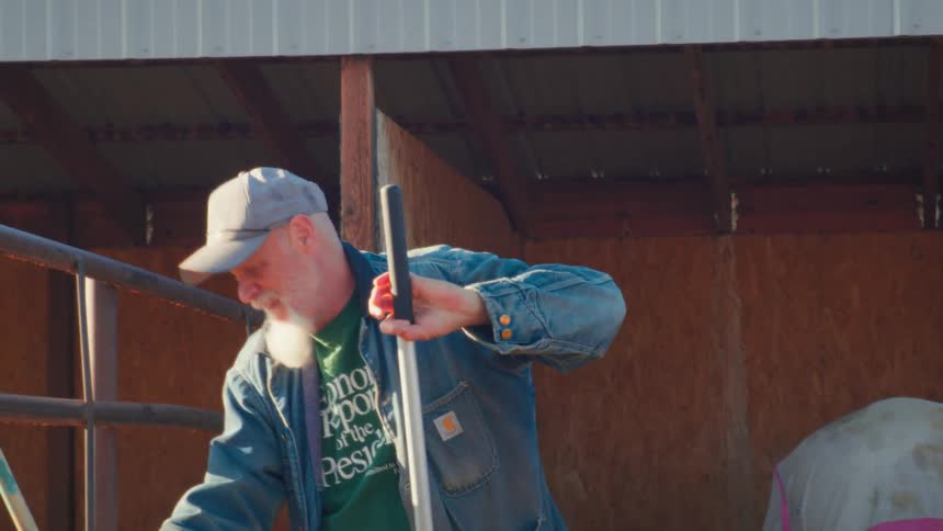 A bearded rancher lovingly pats his horse before starting the chore of cleaning the manure from the stable floor