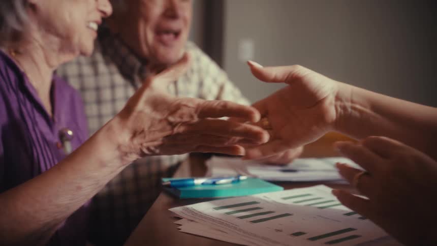 An elderly couple reacts with surprised joy and laughter, shaking hands to celebrate receiving good news during a meeting