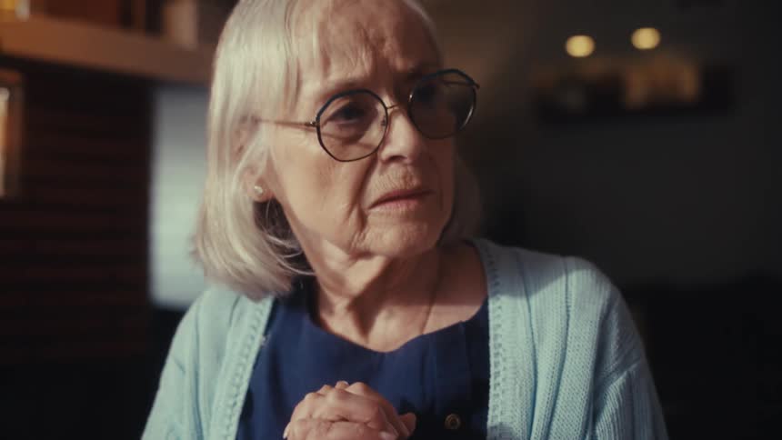 A senior woman listens with a worried and concerned expression while sitting at a table with her husband during a serious conversation