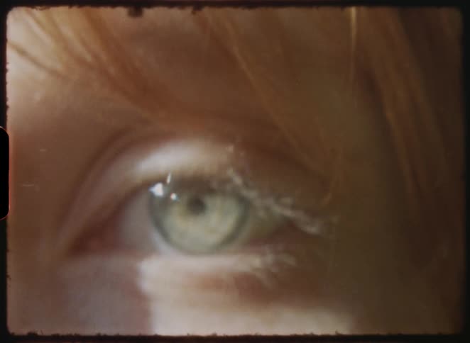 An extreme close-up shot of a person's eye blinking, with a vintage, archival film aesthetic