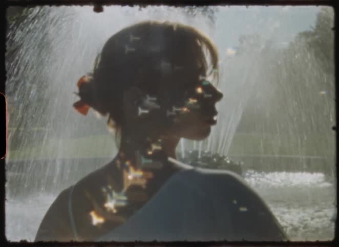Dreamy vintage footage shows the silhouette of a woman posing gracefully before a sunlit water fountain
