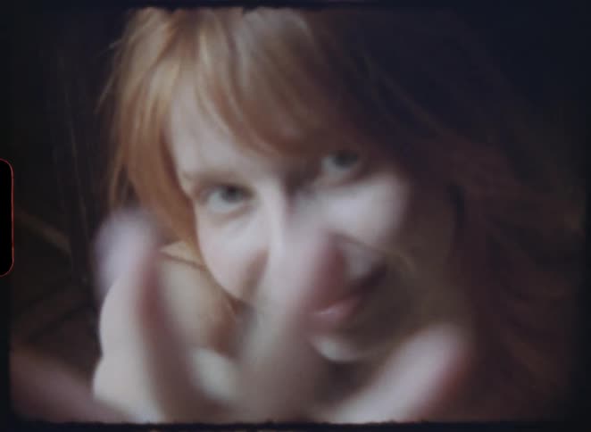 Dreamy, nostalgic footage shows a close-up of a woman with red hair who looks directly at the camera before reaching for it