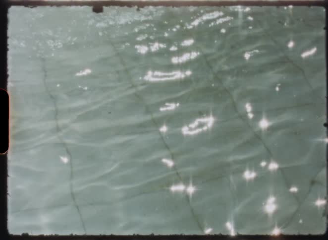 Vintage Super 8 footage shows sunlight sparkling on the rippling surface of a tiled swimming pool