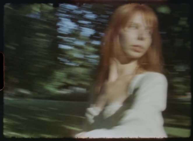 Ethereal vintage-style footage captures a red-haired woman leading her partner by the hand through a sun-dappled park