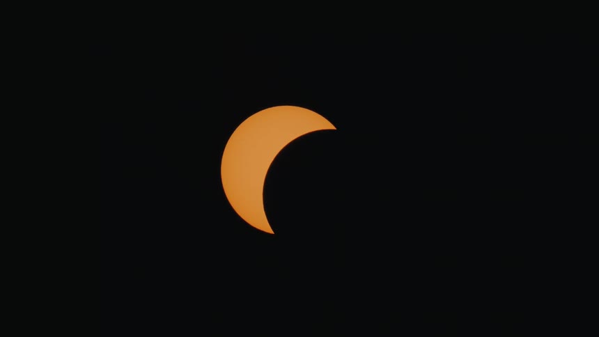 Time-lapse footage captures a partial solar eclipse as the moon slowly obscures the orange sun in the night sky