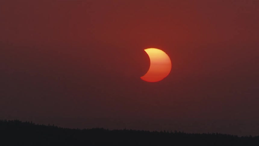 Time-lapse of a partial solar eclipse setting behind a silhouetted forest against a dramatic red sky