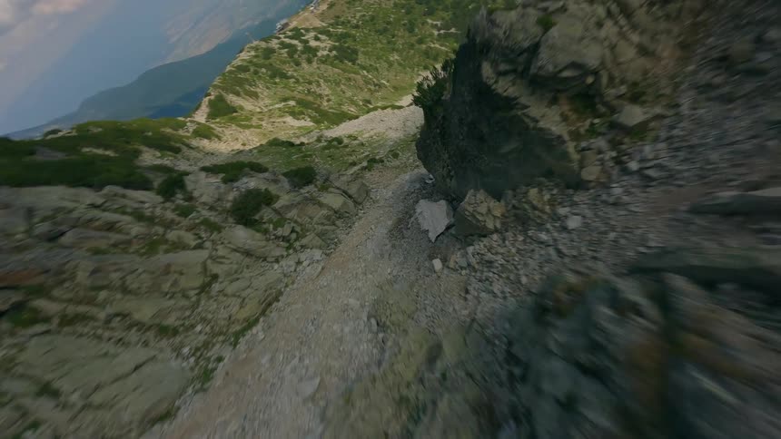 An exhilarating FPV drone flight soars down a rugged mountain cliff and dives into a rocky gorge