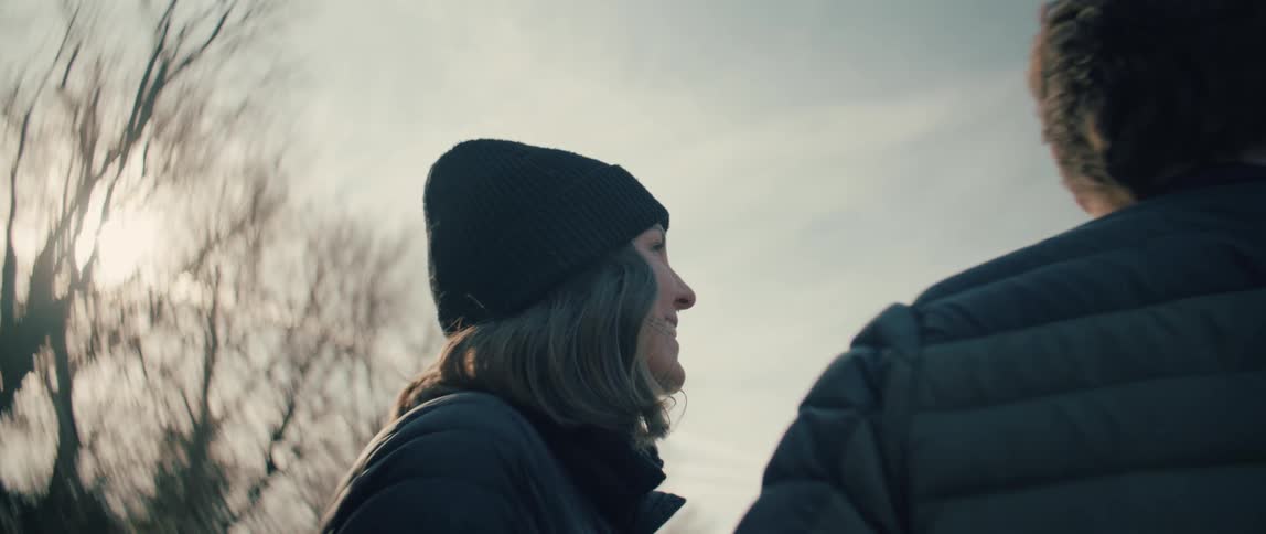 Low angle shot of a smiling woman in a beanie enjoying a conversation with her partner outdoors on a cold day