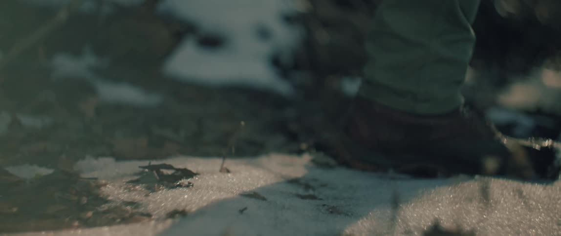 Slow motion close-up of brown leather boots crunching through the snow and fallen leaves on a winter trail