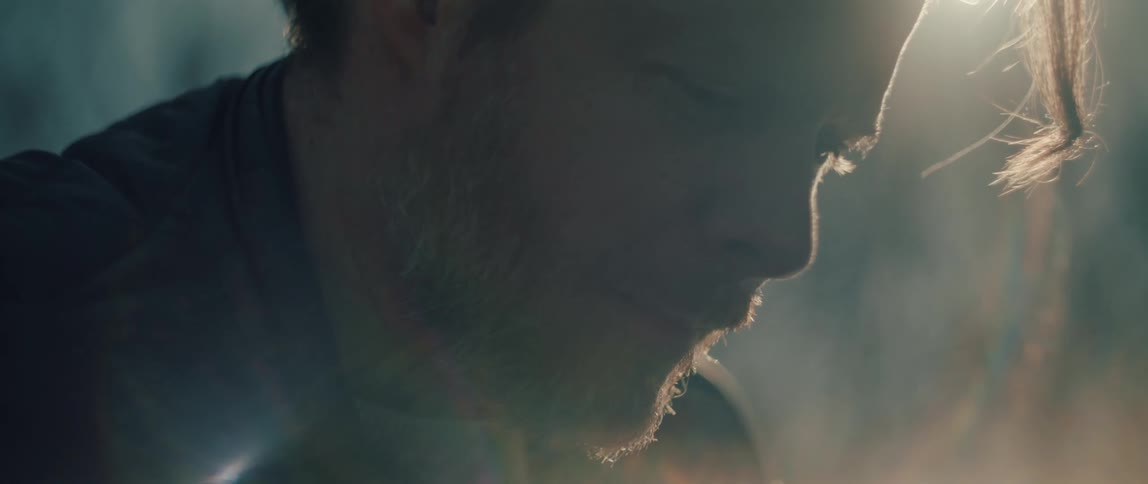 Softly lit close-up of a bearded man's profile as he looks down with a peaceful expression