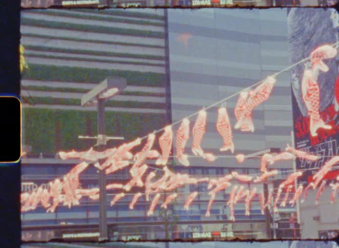 Vintage film footage shows traditional Japanese koinobori carp streamers flying in the wind in a modern city