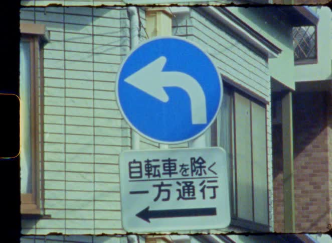 A close-up shot of a Japanese one-way traffic sign with a left-pointing arrow, captured on vintage 8mm film