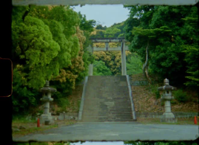 A serene 8mm film shot zooms out from a traditional Japanese stone torii gate at the top of a long staircase in a lush green forest