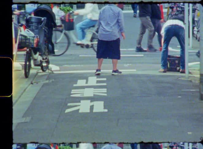 A vintage film-style shot of a Japanese street with people waiting and walking by a 'Stop' sign painted on the road