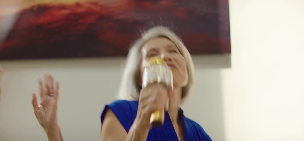 An energetic senior Asian woman sings her heart out into a karaoke microphone during a lively party