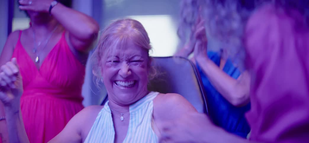 A diverse group of senior women friends laugh and dance with joy in slow motion at a vibrant party