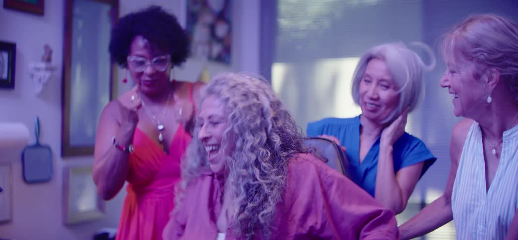 A group of diverse senior women laugh and dance together in celebration at a tattoo parlor