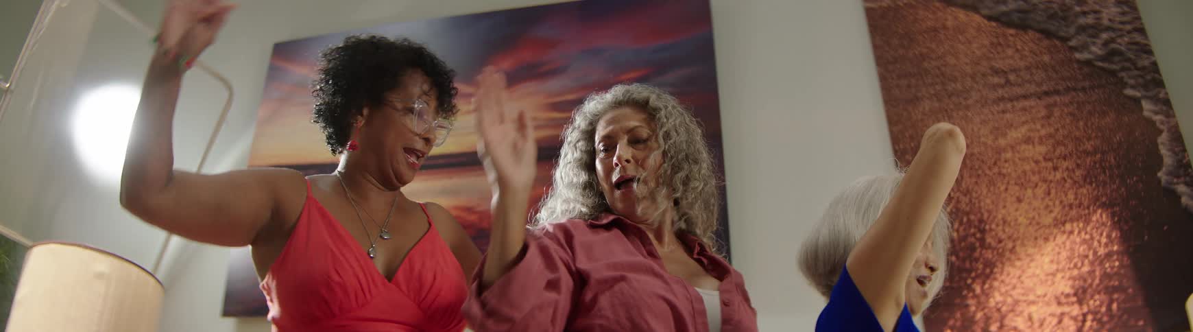 A slow-motion, low-angle view of three exuberant middle-aged women dancing with joy and laughter