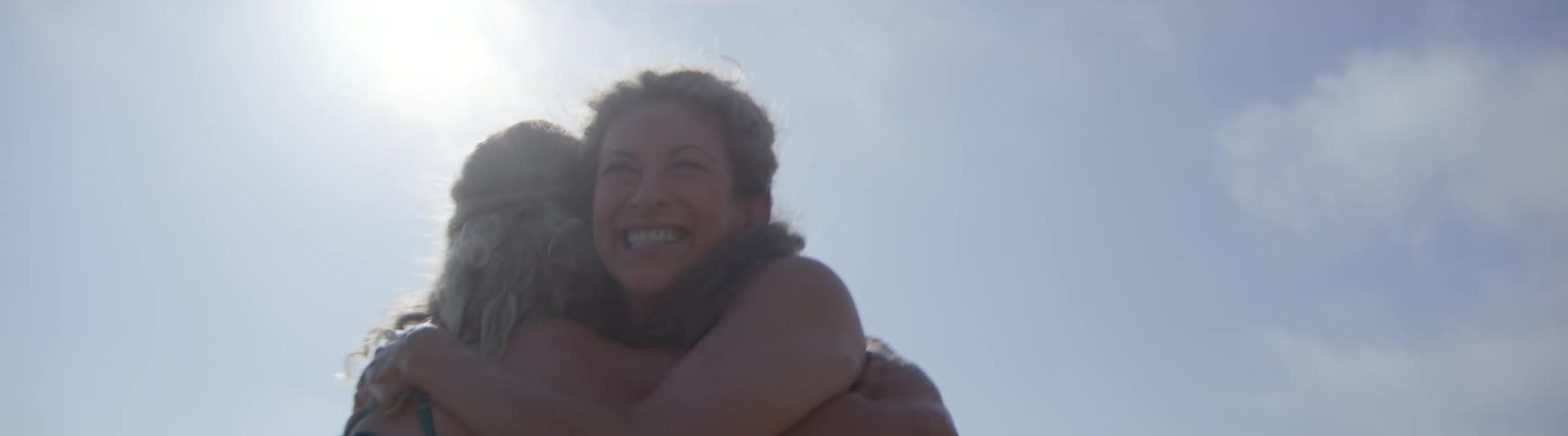 Two happy women run towards each other and embrace in a joyful hug in slow motion on a sunny day