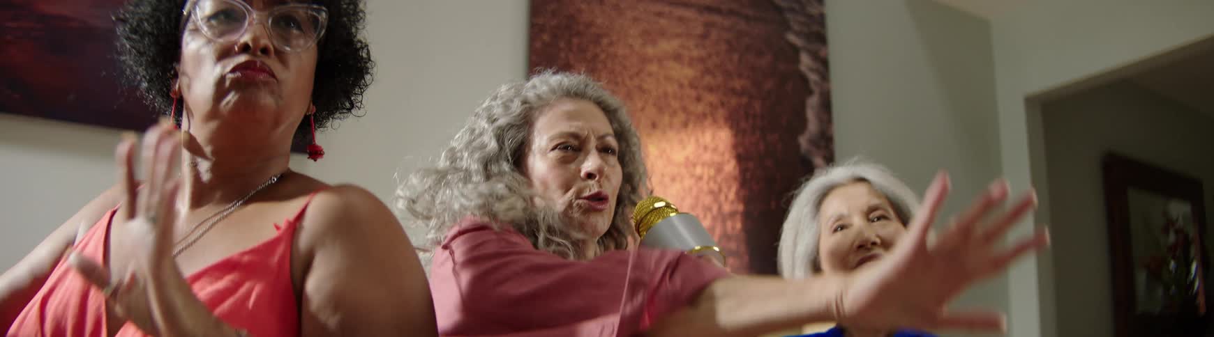 Diverse senior women friends passionately sing and dance during a fun karaoke party in slow motion