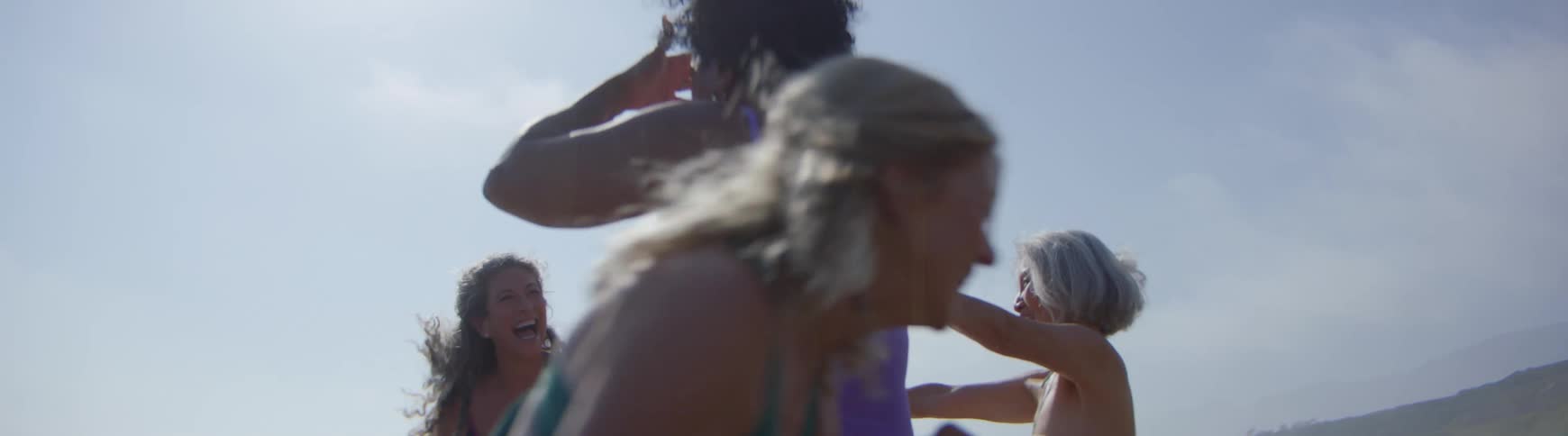 A diverse group of joyful mature women in swimsuits dance and laugh together on a sunny day in slow motion