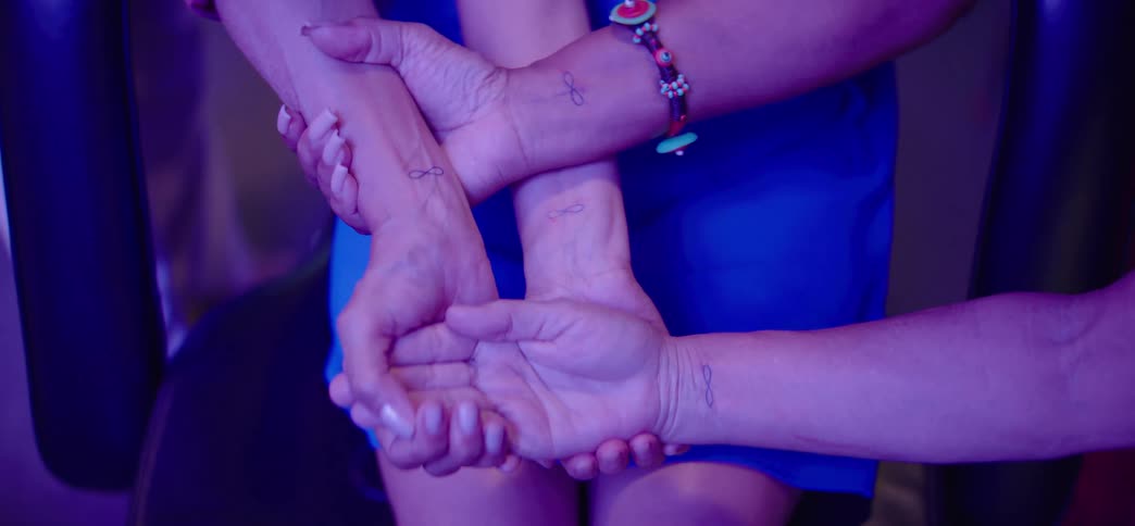 Close-up shot of three people holding hands and wrists, showcasing their identical infinity tattoos