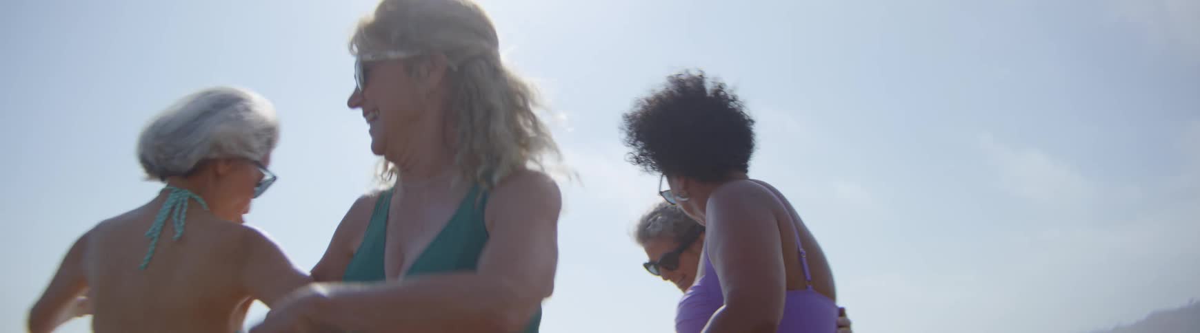 A diverse group of body-positive mature women dance joyfully on the beach in slow motion